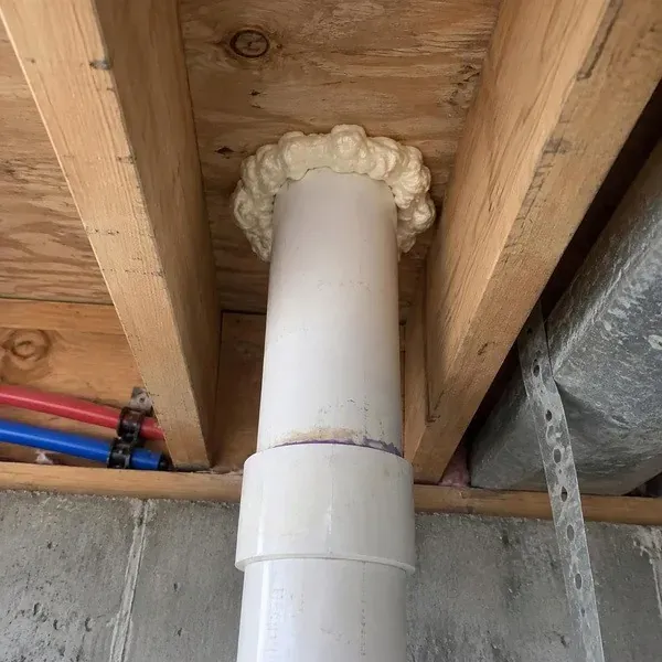 Plumbing penetration sealed with foam where it passes through framing