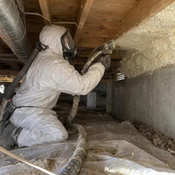 Worker spraying foam inside a narrow crawl space