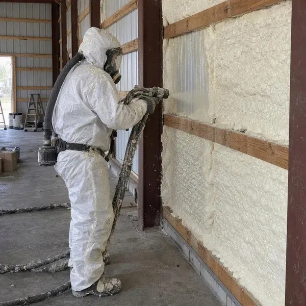 Worker spraying foam along the ribs of a metal building wall