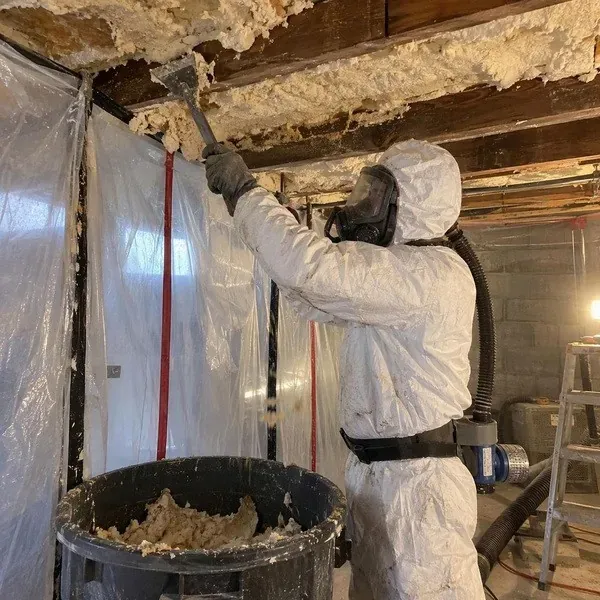 Worker removing old spray foam inside a sealed enclosure